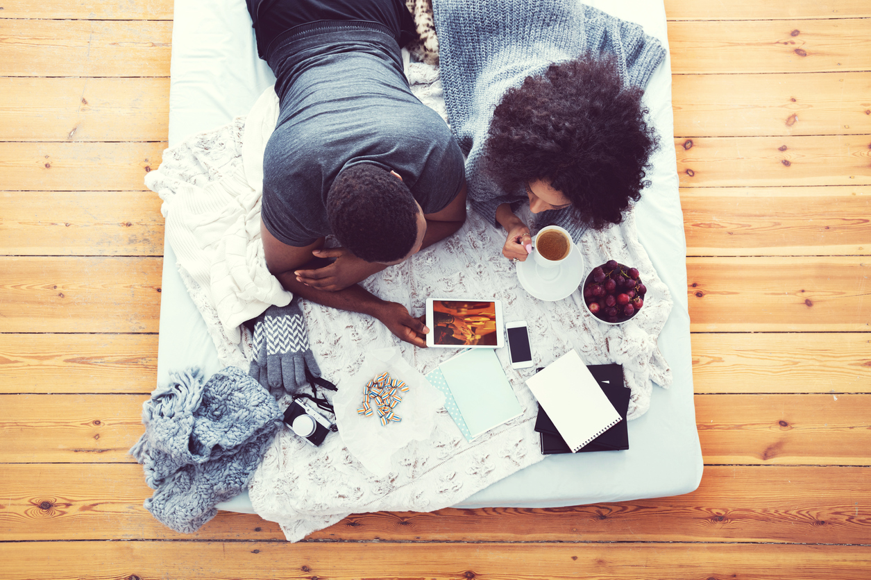 Afro american couple lying on bed and using digital tablet